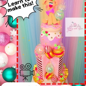May include: A decorative cake with a reindeer figurine on top, featuring pink, white, and gold accents. The cake has multiple layers with striped and spherical decorations. Text includes "Learn to make this!" and "Tutorial".