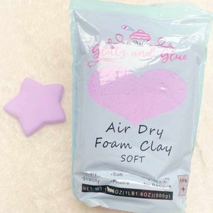 May include: A bag of pink air dry foam clay labeled "Glitts and glue Air Dry Foam Clay SOFT" with a cupcake logo. The bag is on a white fuzzy surface. The clay is soft, pliable, lightweight, and air-dry. It has a net weight of 17.6 ounces (1 pound 1.6 ounces) or 500 grams.