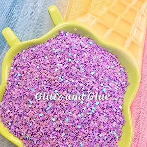 May include: A close-up of a light green, star-shaped dish filled with purple star-shaped glitter. The text "Glitz and Glue" is visible on the glitter. The dish is placed on a colorful background.