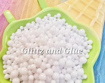 May include: A green, leaf-shaped dish filled with white, spherical beads. The dish sits on a yellow, waffle-textured surface, with a colorful mesh background. The text "Glitz and Glue" is printed on the beads.