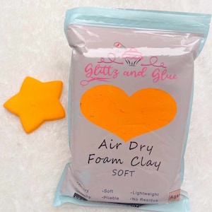 May include: A bag of orange air dry foam clay labeled "Glittz and Glue Air Dry Foam Clay SOFT". The bag is on a white fuzzy surface. The clay is soft, pliable, lightweight, and leaves no residue.