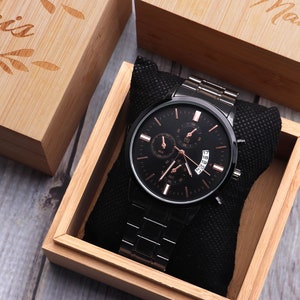 May include: A black watch with a rose gold face and hands, in a wooden box with a black velvet lining. The box is engraved with the word "Man".