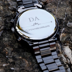 Puede incluir: Reloj de metal negro con una parte posterior plateada grabada con las iniciales "DA" y la palabra "Groomsman".