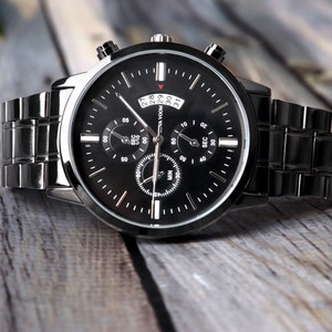 May include: A black chronograph wristwatch with a silver face and black hands. The watch has a date window and a black metal band.