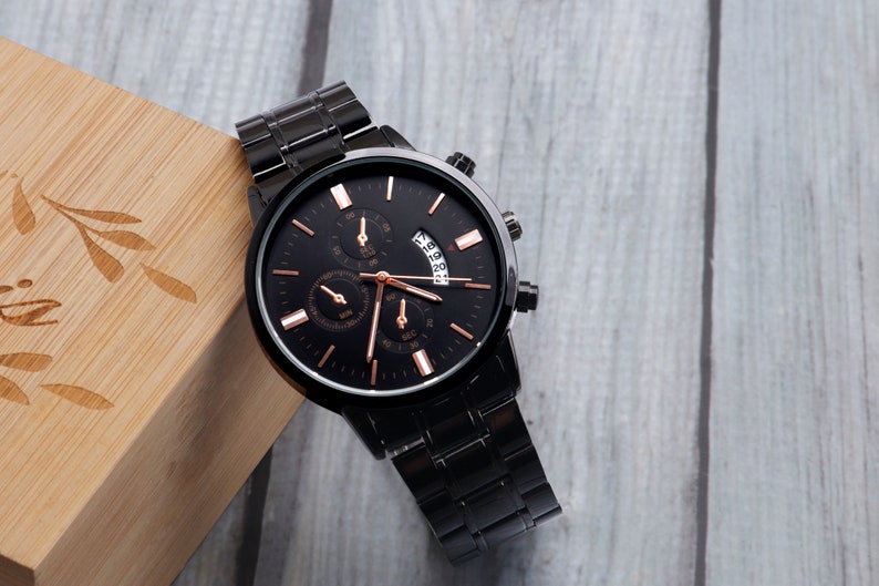 May include: A black wristwatch with a rose gold face and hands. The watch has a black metal band and a date window.