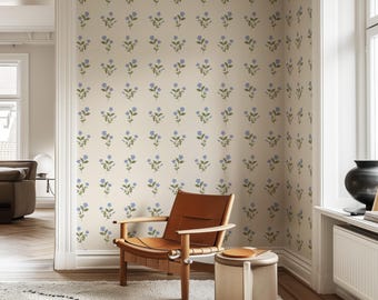 May include: A light brown leather armchair with a wooden frame sits in a room with beige walls covered in a floral wallpaper pattern. The wallpaper features small blue flowers with green stems on a cream background.