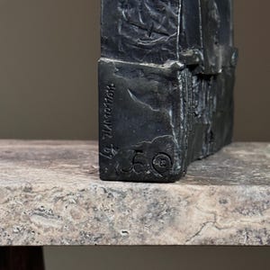 May include: A black metal sculpture with a rough, textured surface. The sculpture is signed "J. Zimmerman" and numbered "50".