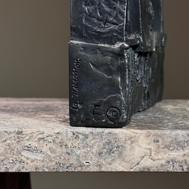 May include: A black metal sculpture with a rough, textured surface. The sculpture is signed "J. Zimmerman" and numbered "50".