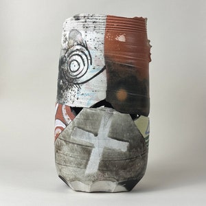 May include: A ceramic vase with a unique, abstract design. The vase is made of brown, white, and black clay and has a textured surface. The vase is broken in two places, but the pieces are still attached.