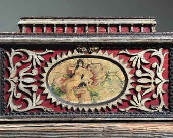 May include: A wooden box with a red and white painted design. The box has a carved oval frame with a painted image of two figures in a flower. The box has a decorative top with a carved design.