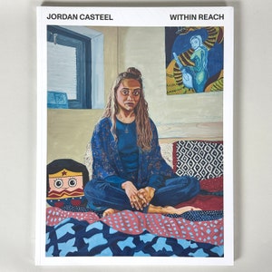 May include: A book cover featuring a painting of a woman sitting on a bed with a colourful quilt. The woman is wearing a blue shirt and a patterned robe. The book title is "Within Reach" and the author is "Jordan Casteel".