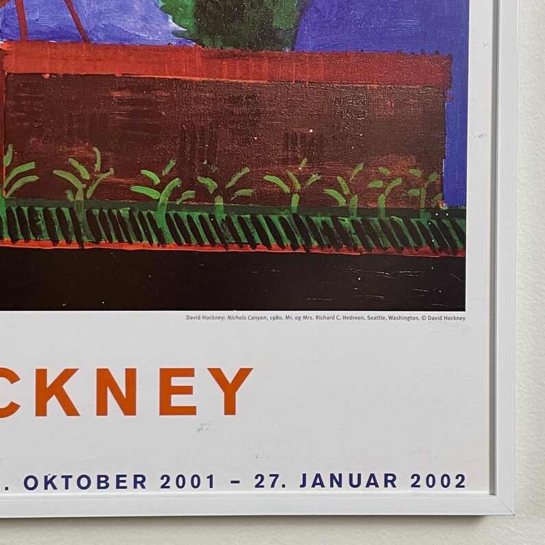 May include: A poster advertising an exhibition of David Hockney's work. The poster features a painting of a house with a red roof and green bushes in front of it. The text on the poster reads "David Hockney: Nichols Canyon, 1980. Mr. og Mrs. Richard C. Hedreen, Seattle, Washington, &copy; David Hockney" and "CKNEY . ОКТО&Beta;ER 2001 - 27. JANUAR 2002".