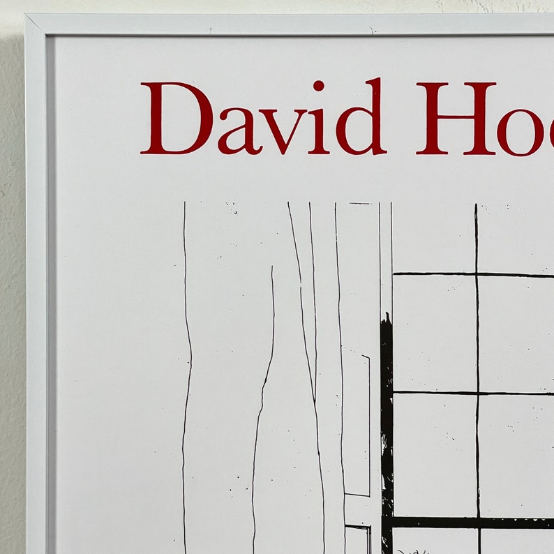 May include: A white framed print with the text "David Hockney" in red lettering. The print features a black and white line drawing of a window with a grid pattern.