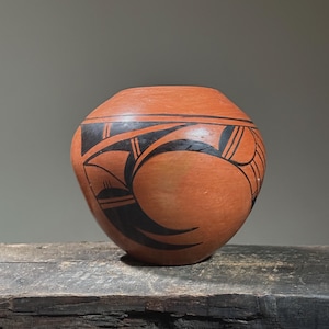 May include: A red clay pottery pot with black geometric designs. The pot is round and has a wide opening.