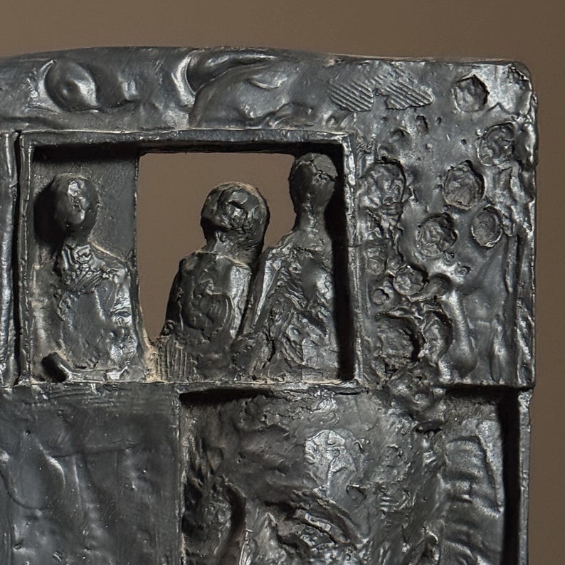 May include: A black and white sculpture of three figures in a rectangular frame. The figures are carved in a rough, textured style, and the background is filled with abstract shapes.