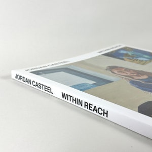 May include: A white book titled "Within Reach" by Jordan Casteel. The book cover features a close-up of a person's face and a painting of a building.
