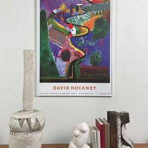 May include: A poster of a painting by David Hockney, featuring a colorful landscape with a winding road, trees, and houses. The poster is titled "David Hockney" and includes the text "Louisiana Museum for Moderne Kunst 12. Oktober 2001 - 27. Januar 2002".