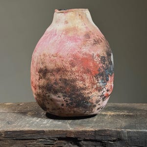 Może przedstawiać: Okrągły, ceramiczny wazon z fakturowaną, marmurkową powierzchnią w odcieniach różowego, czerwonego, brązowego i czarnego. Wazon stoi na postarzanej drewnianej powierzchni.