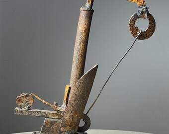 Könnte beinhalten: Eine rostige Metallsculptur mit einem gelben, gebogenen Arm und einem kreisförmigen Element. Die Skulptur hat eine Basis und ein hohes, vertikales Element.