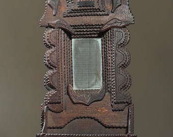 May include: A wooden mirror with intricate carvings and a small drawer. The mirror is framed in a dark brown wood and has a simple, rectangular shape. The carvings are detailed and create a decorative border around the mirror.