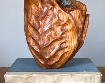 May include: A wooden sculpture of a stylised wave with a metal beetle on top. The sculpture is sitting on a stack of books.