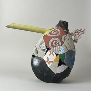 May include: A ceramic pitcher with a long, yellow spout and a patchwork design. The pitcher is decorated with various colors and patterns, including circles, swirls, and geometric shapes.