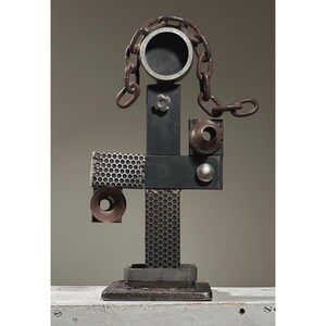 Könnte beinhalten: Abstrakte Metallskulptur in Form einer Figur. Sie integriert industrielle Komponenten wie eine Kette, Lochblech und zylindrische Formen. Die Farbpalette ist metallisch, mit Schattierungen von Braun und Grau.