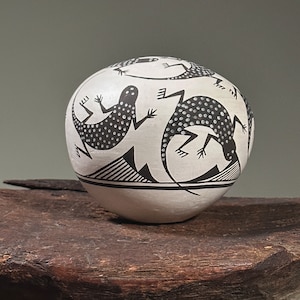 Puede incluir: Una maceta de cerámica blanca con un diseño en blanco y negro de tres lagartos. Los lagartos son estilizados y tienen manchas negras.
