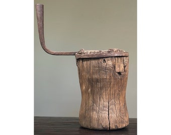 Puede incluir: Un cubo de madera rústico con un asa de metal. El cubo está hecho de madera toscamente labrada y tiene un acabado natural y desgastado. El asa de metal está unida a la parte superior del cubo y está doblada en forma de curva.