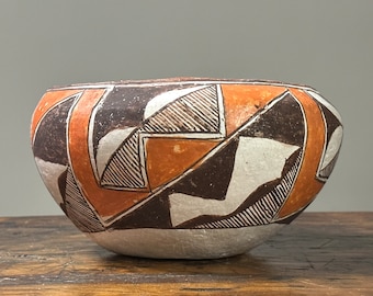 Puede incluir: Un cuenco de cerámica tradicional nativo americano con un diseño geométrico en negro, blanco y naranja. El cuenco es redondo y tiene un borde ligeramente acampanado.
