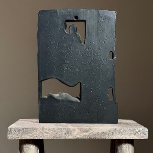 May include: A black abstract sculpture with cutouts, resembling a figure and a shape, on a light gray stone pedestal.