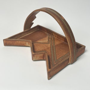 May include: A brown ceramic serving tray with a geometric design and a handle. The tray has a unique shape with a zig-zag edge.