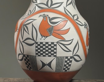 May include: A white ceramic pot with a geometric design featuring black and orange accents. The pot is decorated with a stylized bird and leaves.