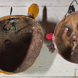 Puede incluir: Dos m&aacute;scaras vintage de papel mach&eacute; con detalles pintados. Una m&aacute;scara es amarilla con detalles marrones y verdes, la otra es roja con detalles marrones. Ambas m&aacute;scaras tienen un interior hueco.