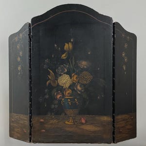 May include: A three-panel folding screen with a dark background and a painted floral still life. The flowers are in a blue and gold vase. The screen has a curved top and decorative accents.