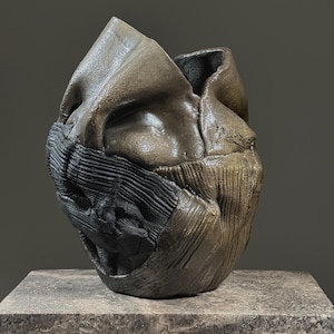 May include: A ceramic sculpture with a textured, abstract design. The sculpture is brown and black and has a rough, organic feel.