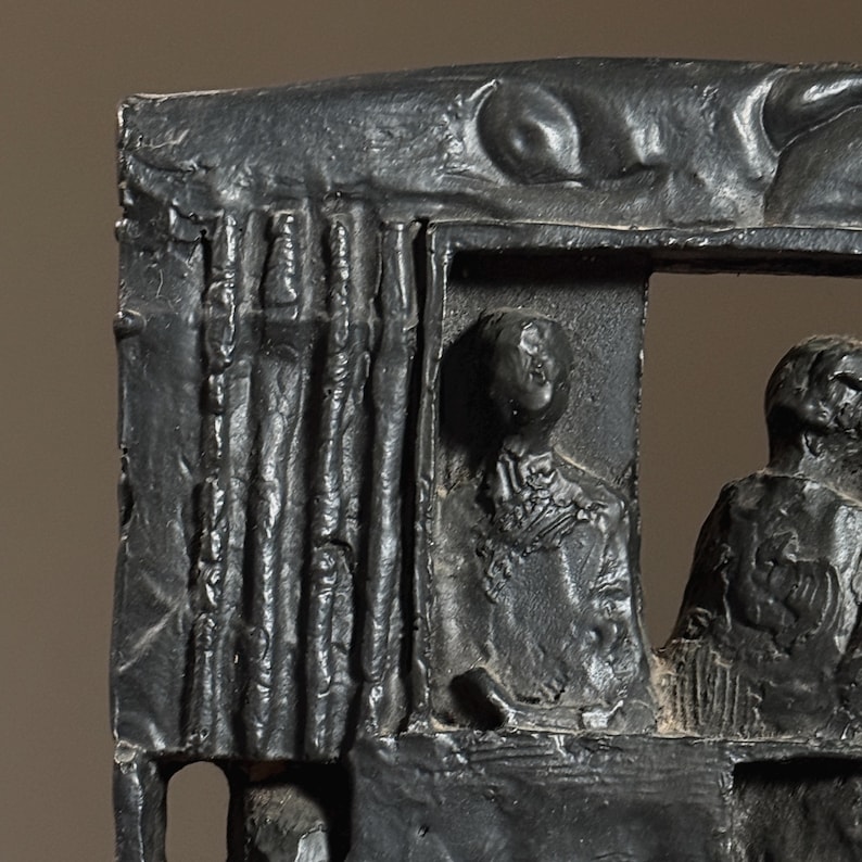 May include: A black and white sculpture of three figures. The figures are in a window-like frame. The sculpture is made of a rough, textured material.