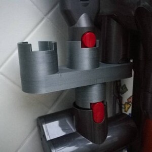 May include: A gray plastic wall mount with two slots for holding vacuum cleaner attachments. The slots have red buttons.