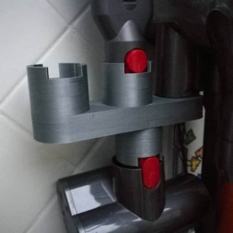 May include: A gray plastic wall mount with two slots for holding vacuum cleaner attachments. The slots have red buttons.