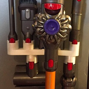 May include: A white plastic wall mount with red and gray attachments for a cordless vacuum cleaner and its accessories. The vacuum cleaner has a purple and gray head with a red button.