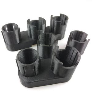 May include: A black plastic battery holder with six slots for batteries. The holder is designed to hold batteries in a vertical position.