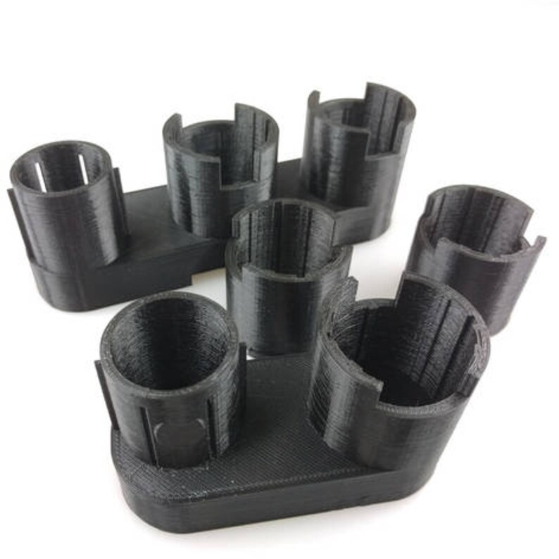 May include: A black plastic battery holder with six slots for batteries. The holder is designed to hold batteries in a vertical position.