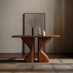 Puede incluir: Una consola de madera moderna con una base curva única. La mesa es de color marrón cálido y tiene una parte superior rectangular. Está adornada con un jarrón con ramas secas, un candelabro y dos botellas pequeñas. La mesa mide aproximadamente 150 cm de largo.