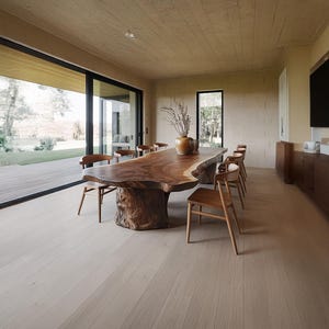 May include: A large, live-edge wooden dining table with a natural, organic shape. Surrounding the table are several wooden chairs. The room has light-colored wood flooring and a large window overlooking a natural landscape.