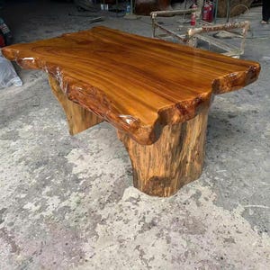 May include: A handcrafted wooden table with a natural edge. The tabletop is a rich, glossy brown, supported by a base made from a tree trunk. The table's unique design adds a rustic and organic feel to any space.
