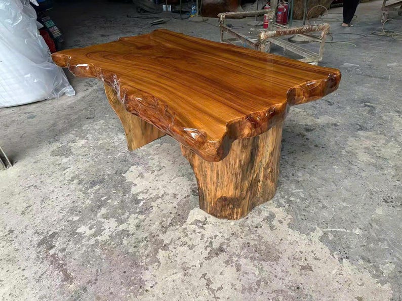 May include: A handcrafted wooden table with a natural edge. The tabletop is a rich, glossy brown, supported by a base made from a tree trunk. The table's unique design adds a rustic and organic feel to any space.
