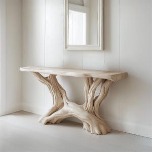 May include: A light-coloured wooden console table with a natural, organic design. The table has a long, rectangular top supported by a base crafted from intertwined, branch-like structures. The table is set against a white wall with a mirror.