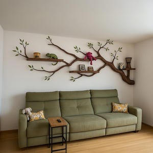 Könnte beinhalten: Ein Wohnzimmer mit einem grünen Sofa, einem kleinen Beistelltisch aus Holz und einem wandmontierten, baumförmigen Regal. Das Regal zeigt verschiedene dekorative Gegenstände, darunter eine grüne Eidechse, ein rosa Stofftier und kleine gerahmte Bilder.