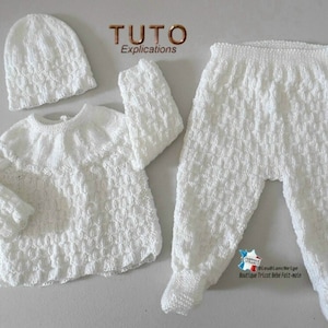 May include: White knitted baby outfit set with a hat, sweater, and trousers. The set features a textured stitch pattern.