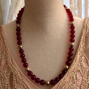 May include: A red and gold beaded necklace. The necklace is made of round, red glass beads with gold accents.